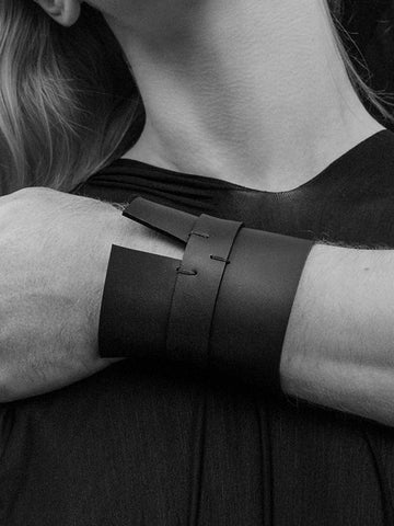 Person modeling black leather cuff jewelry worn on wrist, set in black and white.