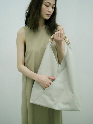 Person with long black hair pictured holding an ivory Kamaro'an bag against a neutral backdrop.