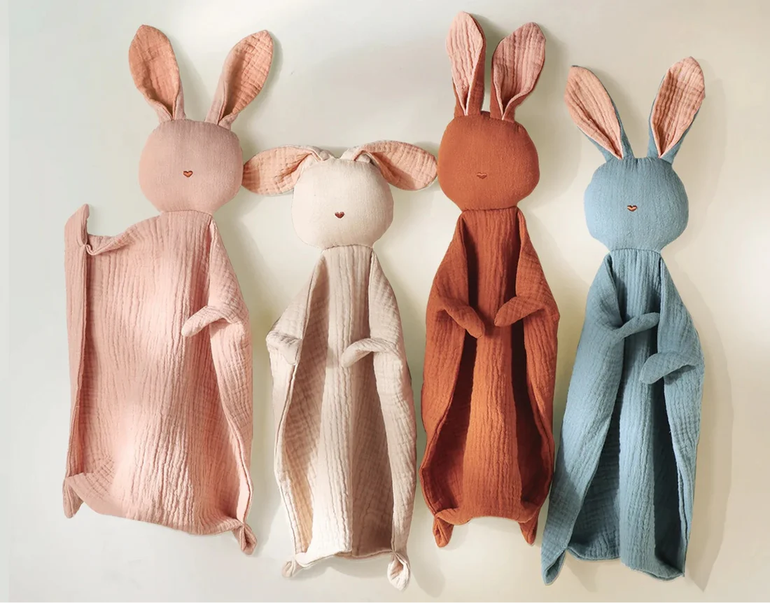 Quatre Doudous Lapin de couleurs variées (rose, crème, rouille, bleu) suspendus