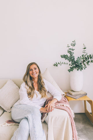 Jessica Brickenden, founder of Taylor & Gray and online Irish homewares and furniture shop, pictured sitting on a farmhouse style couch, with a ceramic vase and eucalyptus, as well as linen cushions and a soft throw for a couch.
