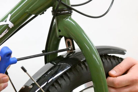 A mechanic uses a screwdriver on the other side of the fork to install a fender flute