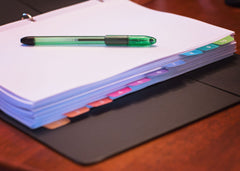 A photo of a binder filled with papers and dividers with a green pen sitting on top of the papers.