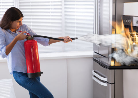 woman putting out fire in kitchen with extinguisher