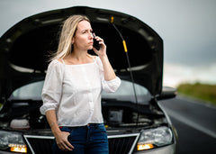 woman on cell phone standing in front of her broken down car