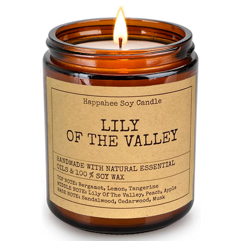 A gently flickering Lily of the Valley scented candle from Happahee, in an amber jar with a sticker, on a white surface, offering a crisp, springtime scent to Dubai homes.