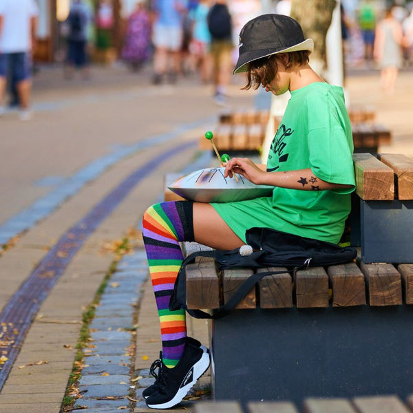 adolescent branché jouant du tongue drum sur un banc dans une rue touristique