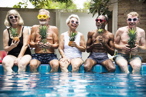 Adults dipping their feet at a pool with funny sunglasses and pineapples