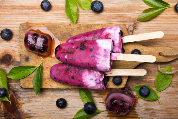 homemade blueberry popsicles stacked on a wood cutting board with ice melting in the summer heat. 