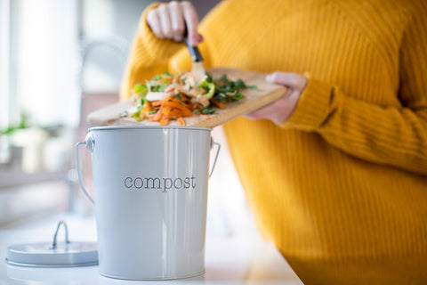 A woman in a yellow sweater putting her leftovers into a metal compost bin
