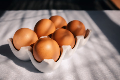 Picture of half a dozen eggs resting inside a white ceramic egg holder