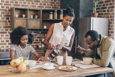 A beautiful family having breakfast while the mother pours coffee out of her french press.