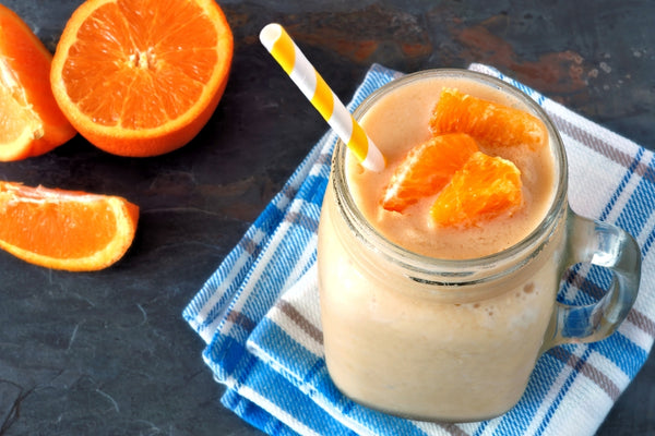 Un smoothie orange avec de la poudre de protéines végétaliennes sur un comptoir gris foncé