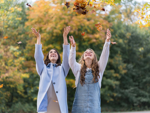 Two friends smiling while they toss fall leaves into the air. They are thankful to be alive.