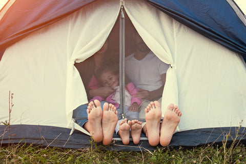 Summer Glamping Family Road Trip with two pairs of adult feet sticking out of a tent and one pair of children's feet. 