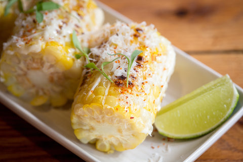 Elote, small cut corncobs on a dish with seasoning and lime. 