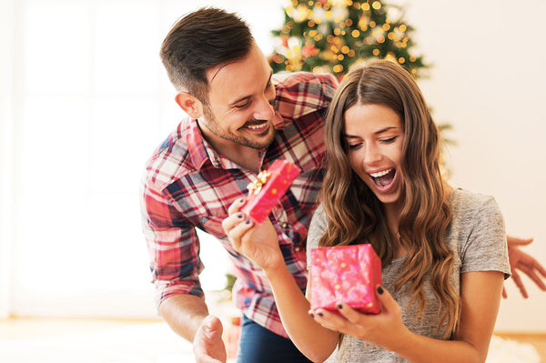 A woman smiling with joy as she opens a present gifted to her by her male partner