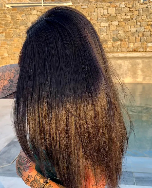 Person with long, straight black hair standing outdoors by a stone wall.