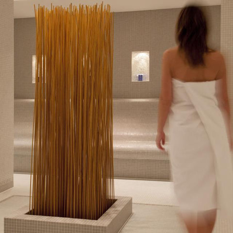 White steam room, woman with towel over her body and wooden art installation