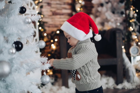 Un enfant avec un bonnet rouge touchant un sapin blanc