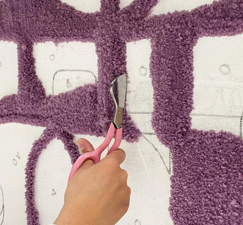 Hand holding a pair of pelican scissors on a tufting canvas