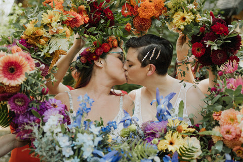 Two brides with a ring of bridesmaid bouquets in rainbow colors by florist Gorgeous and Green for Yosemite wedding Evergreen Lodge Photo by Julia Mina