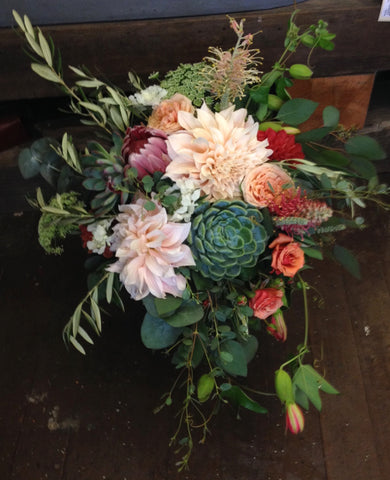 Beautiful bridal bouquet in coral and peach by Gorgeous and Green featuring local grown dahlias, succulents, garden roses, passion vine, olive, protea and other textures.