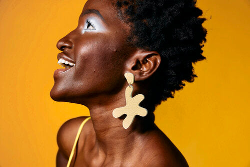 a woman smiles while wearing oversized, star-shaped disco earrings in white authentic leather in butter yellow