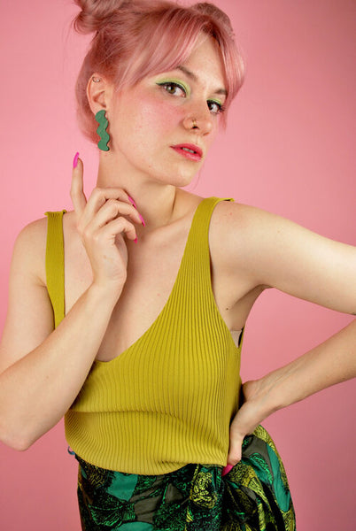 Shelby wears forest green zig zag shaped earrings with a lime green top and lime print wrap skirt with bright green eyeshadow. 