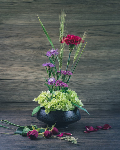 A floral display of purple, burgundy and red fresh flowers, with ears of wheat and fresh green foliage