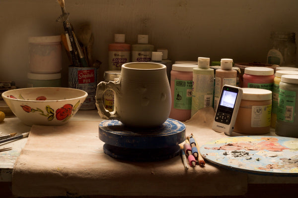 Image of a table with glazes and a mug being worked on a banding wheel