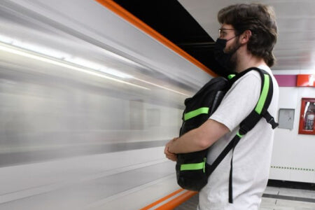 Hombre esperando el metro con su mochila puesta en el pecho.