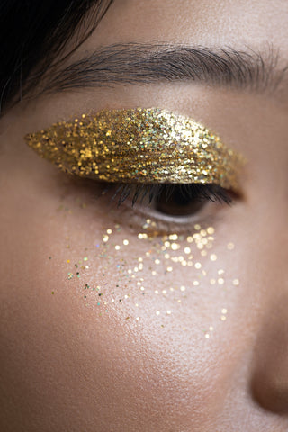 a close up of an asian woman with gold glitter eyeshadow