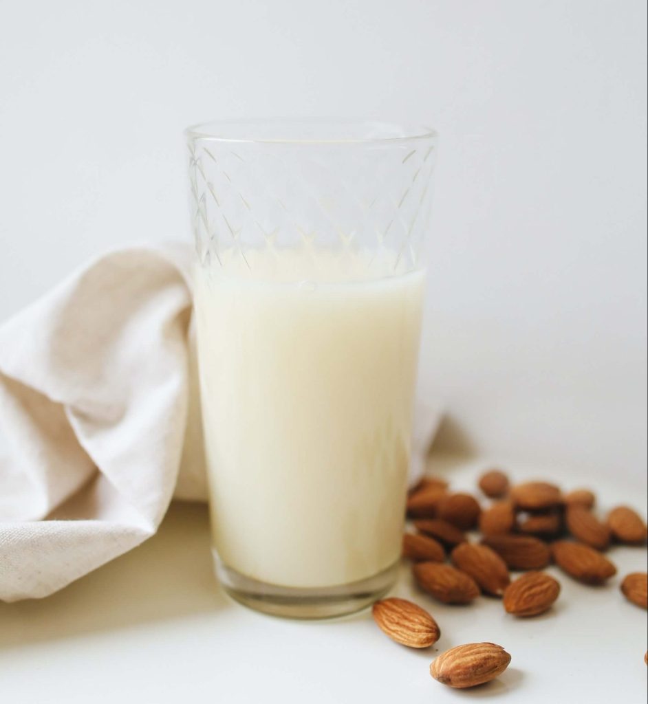 Almond milk in glass with almonds next to it