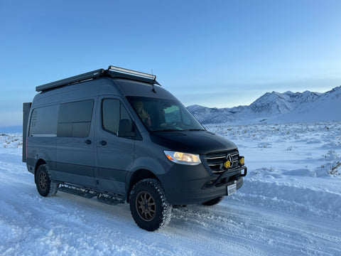 sprinter van driving on snow in front of snowy mountains