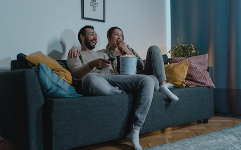 A man and woman sitting on the couch eating popcorn and watching TV