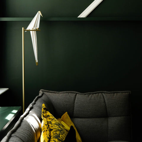 Corner of a room with evergreen colored walls, a lamp that looks like a parrot, and a gray couch with a yellow pillow