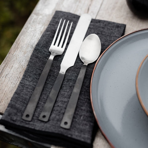 A flatware set by Barebones sitting on a cloth napkin on a patio table.