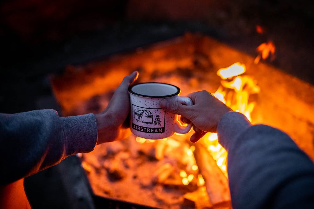 A person holding a coffee mug next to the campfire at night