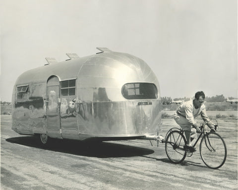 A man towing an Airstream with a bike in a vintage photo