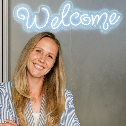 A woman standing in front of a 'Welcome' sign.
