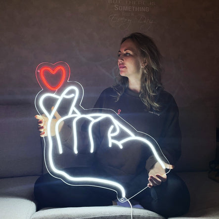 A woman holding a heart-shaped neon hand sign.