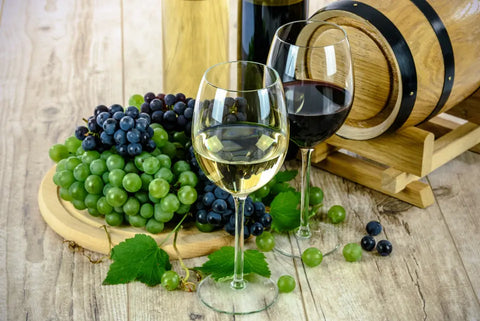 Rotwein und Weißweinglas vor einem Weinfass und und roten und weißen Weintrauben