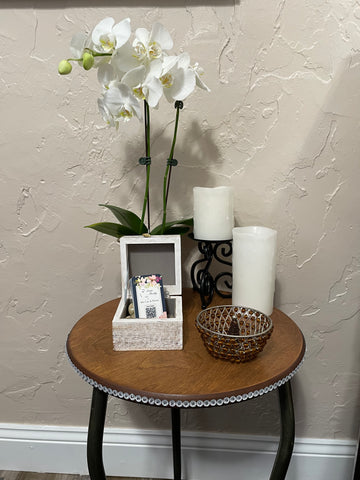A lovely white orchid sits on a circular wooden table with rhinestones around the edge.