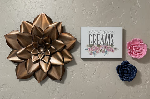 Chase your Dreams pink and blue picture hangs on the wall beside a metal copper lovely flower artwork.