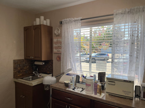 A lovely treatment room with a sink.  The cabinet is painted with a copper metallic color with a copper and gray backsplash over looking the parking lot.