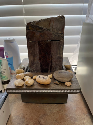 A stone fountain with rhinestones on the edge sits on the countertop and has decorative rocks on it.