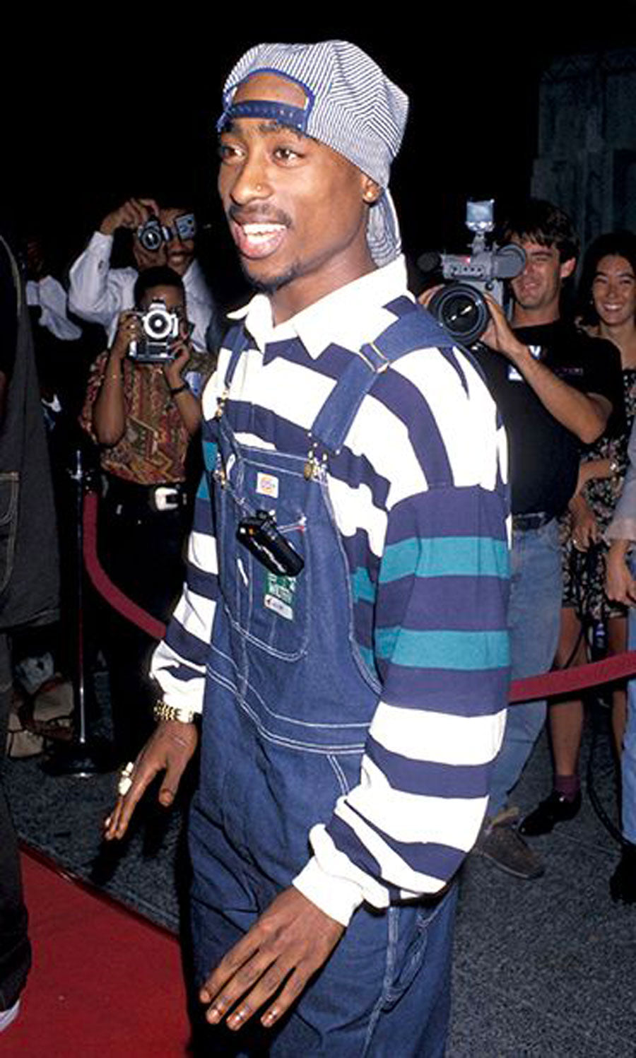 2Pac Shakur in casual street good guy look with denim overalls over blue and white striped long sleeve polo shirt