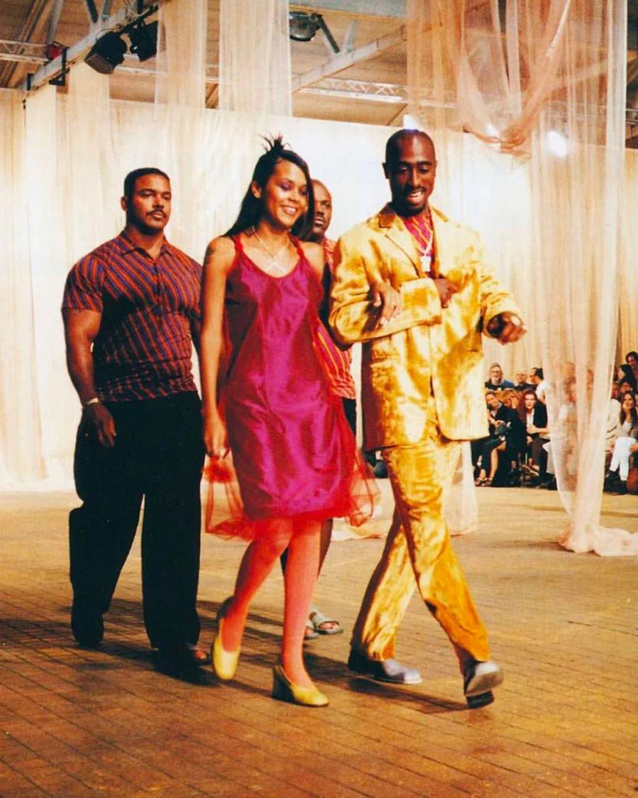 Tupac Shakur e Kidada Jones con look high fashion con completo Versace in velluto dorato ad una sfilata di moda