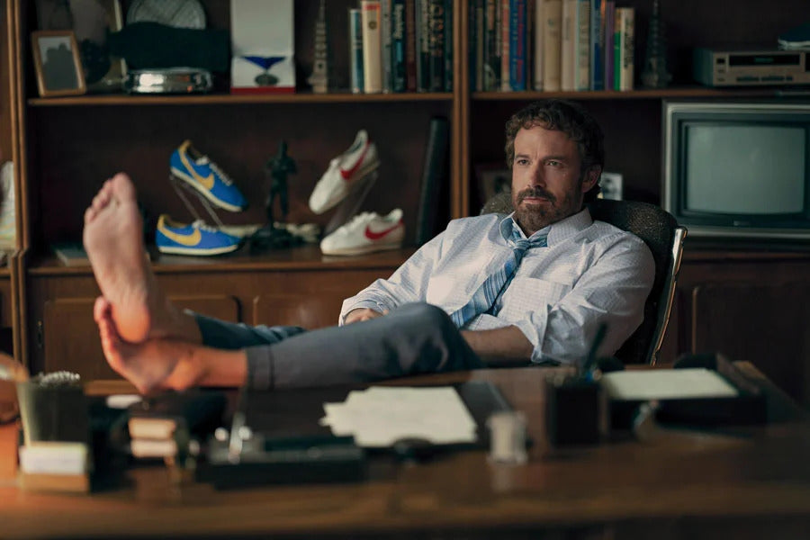 Scene from the film Air: the story of the great leap in which Phil Night, founder and CEO of Nike, played by Ben Affleck, is sitting with his bare feet on the table