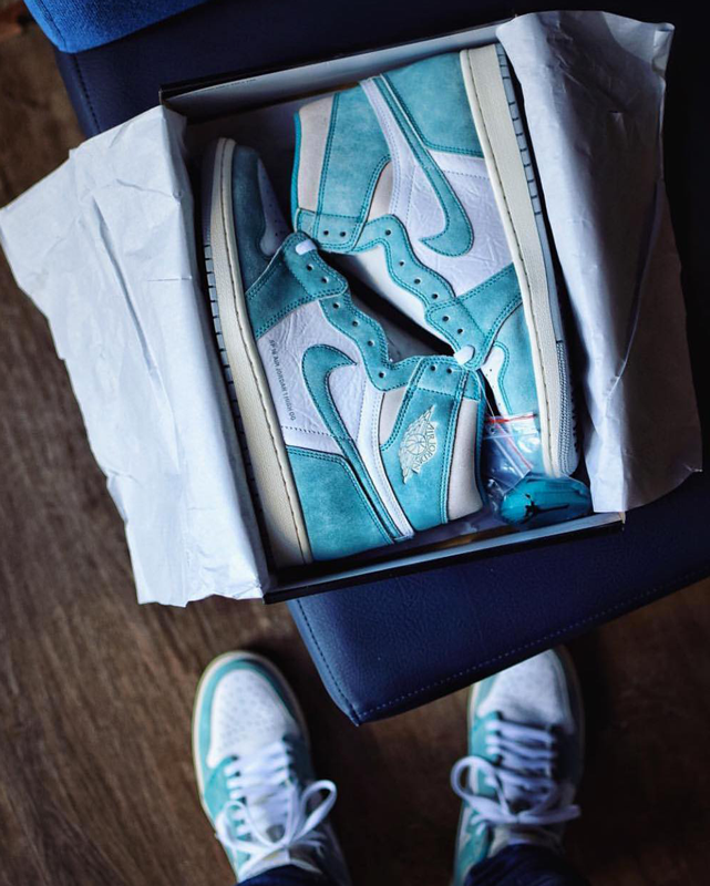 New blue Nike Air Jordan 1 sneakers still in the original box, same as the pair worn by the person taking the photo. A double up